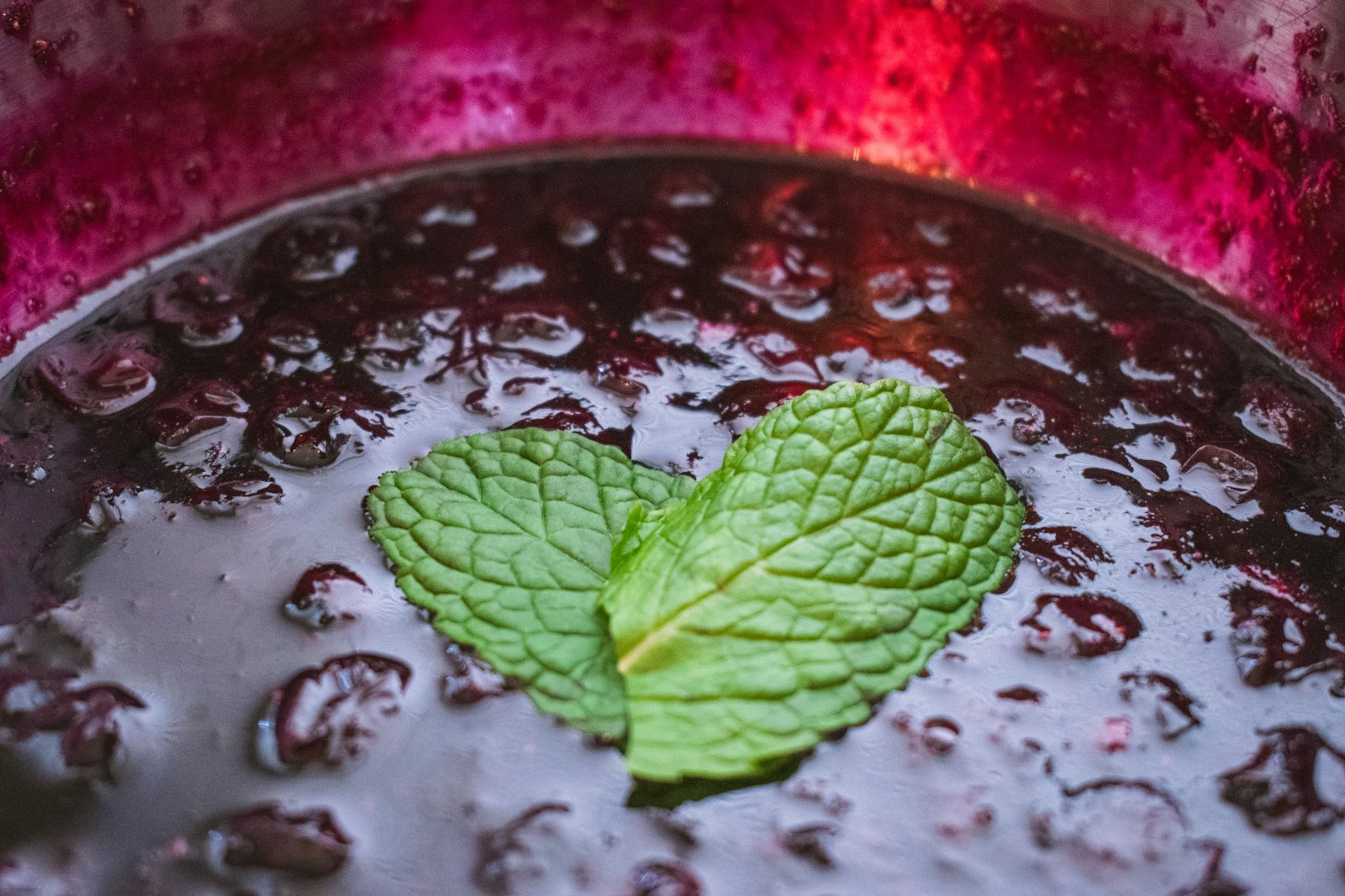 Blueberries cooked down into a soft, glossy compote in a pan, topped with a mint leaf.