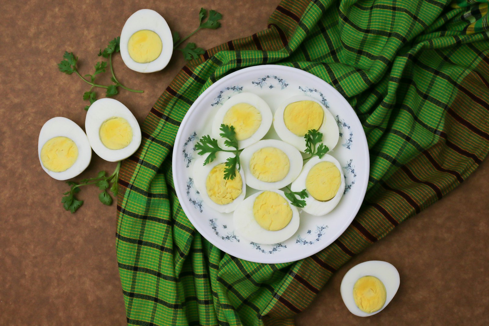 Halved hard-boiled eggs arranged on a small white plate with parsley, on a green checked linen and warm brown surface.